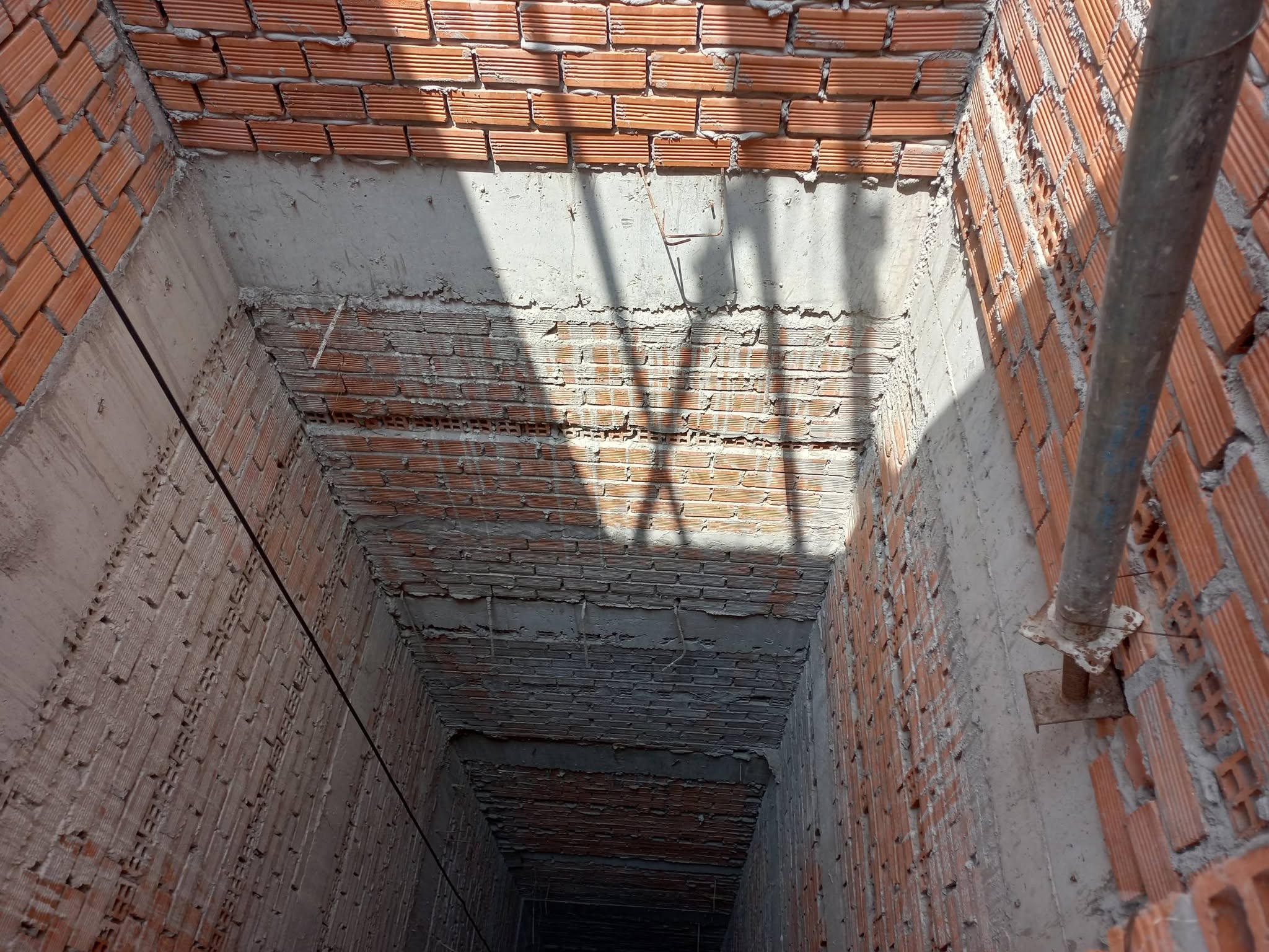 Góc nhìn dọc lòng giếng thang đang xây với tường gạch và các dải bê tông