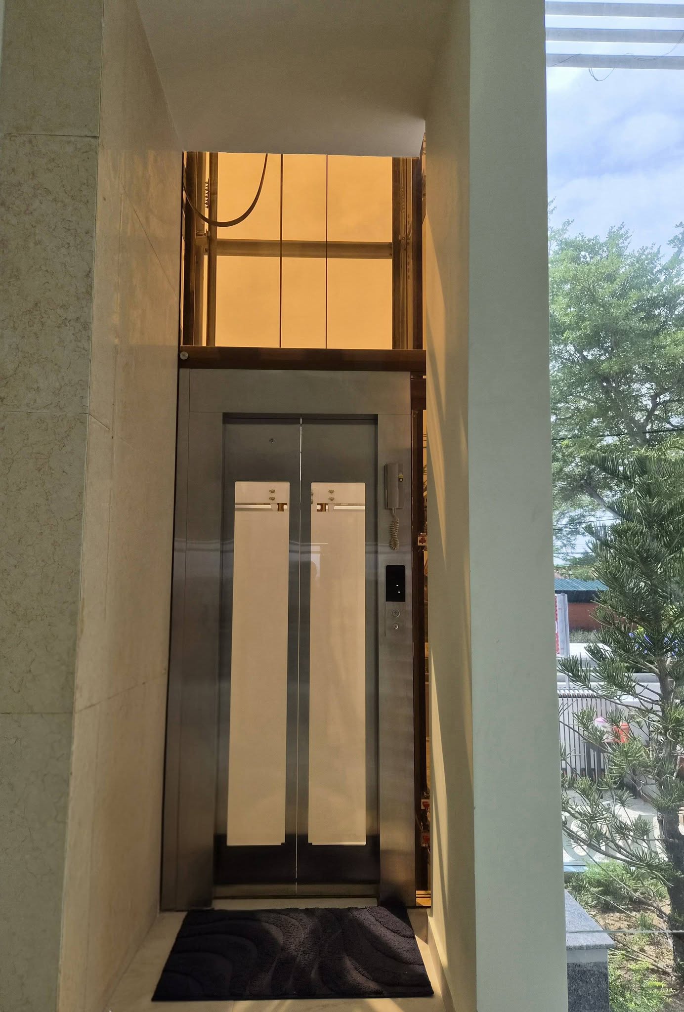 Cửa tầng thang máy ngoài trời với hai ô kính dọc và bảng gọi tầng bên cạnh